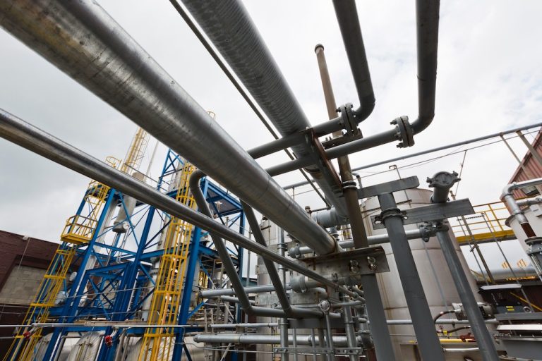 Complex network of industrial pipes at a chemical manufacturing plant with safety railings and scaffolding. Customer Success Story: Ethylene Glycol Recycling.